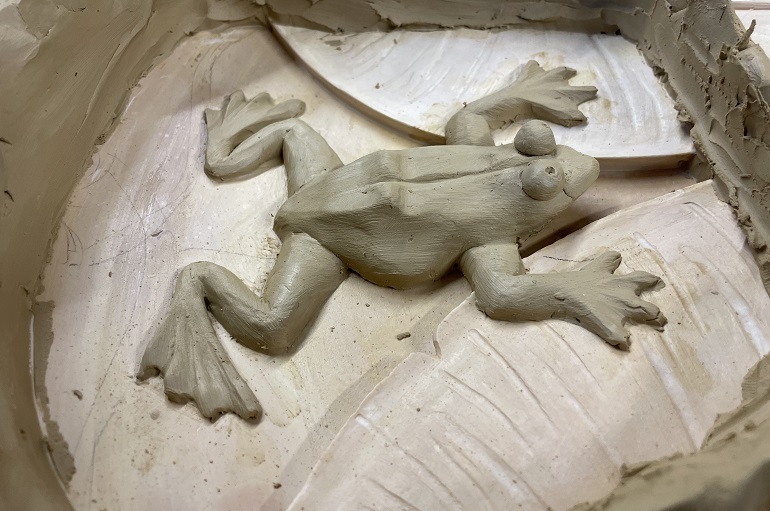 Close-up van handgemodelleerde kikker tijdens het maken van de Art Nouveau rozet